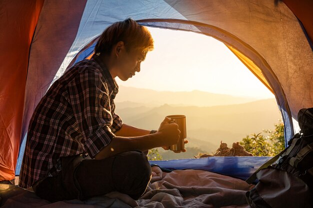 A young man sitting in the tent with holding coffee cup