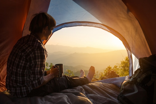 Free photo a young man sitting in the tent with holding coffee cup