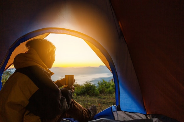 Free photo a young man sitting in the tent with holding coffee cup