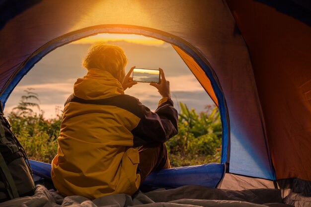 A young man sitting in the tent with taking photo with a mobile phone