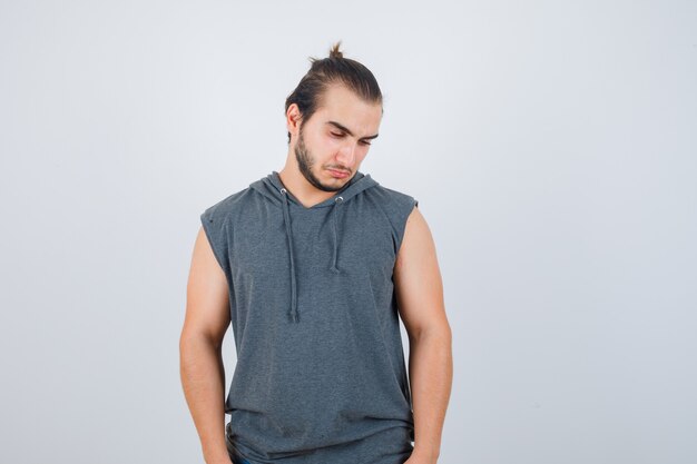 Young man in sleeveless hoodie looking down and looking downcast , front view.