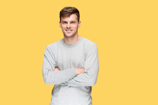 young man smiling and looking at camera on yellow studio background