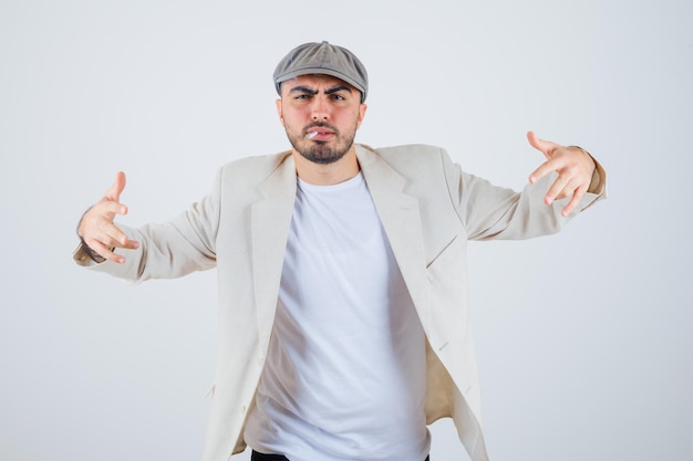 Young man smoking cigarettes and stretching hands toward front in white t-shirt, jacket and gray cap and looking angry