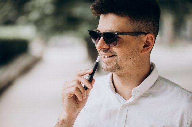 Young man smoking electro cigarette outside in park