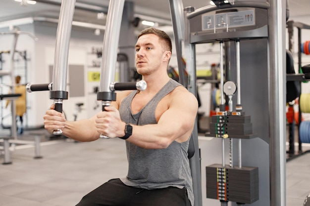 Young man in sportswear doing excercisses on special equipment at gym