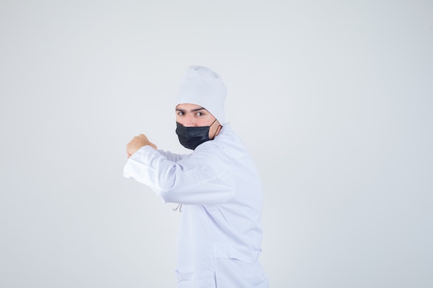 Young man standing in fight pose in white uniform, mask and looking determined . .