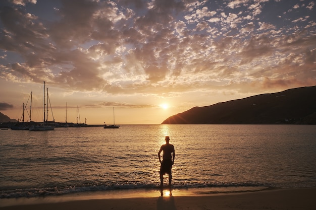 Young man standing in front of the sea in Amorgos island, Greece at sunset