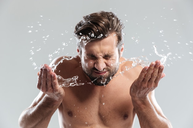 Young man standing isolated over grey wall washes face