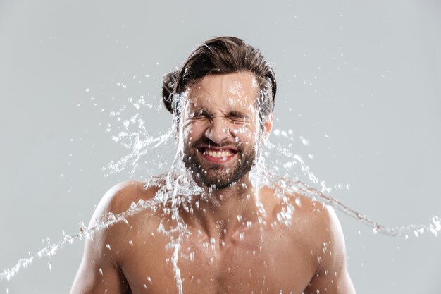 Young man standing isolated over grey wall washes face