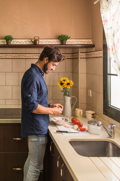 Young man standing in kitchen preparing salad