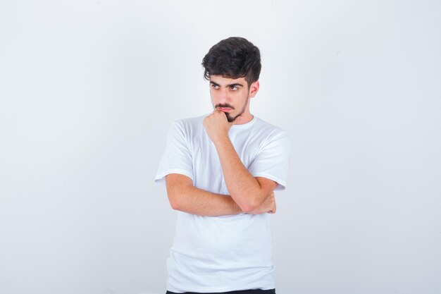 Young man standing in thinking pose while looking away in t-shirt and looking pensive