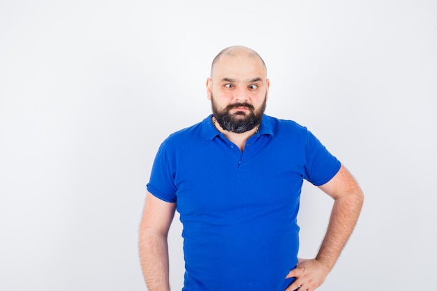 Free photo young man standing while squinting eyes in blue shirt and looking weird , front view.