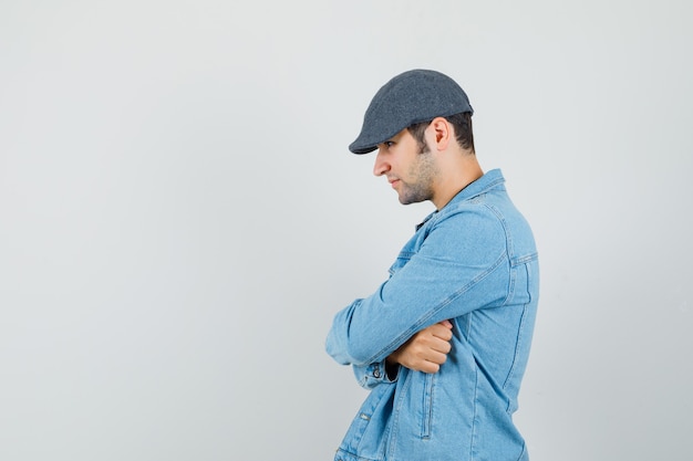 Free photo young man standing with crossed arms in jacket,cap and looking calm. . space for text