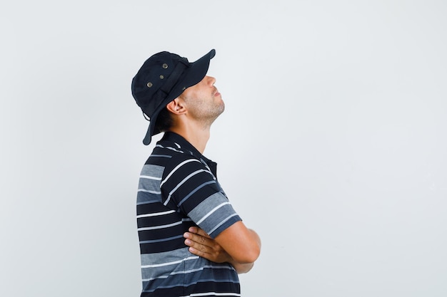 Free photo young man standing with crossed arms in t-shirt, hat and looking pensive .