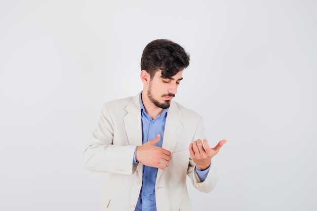 Young man stretching hands as holding something and looking at it in blue shirt and white suit jacket and looking focused