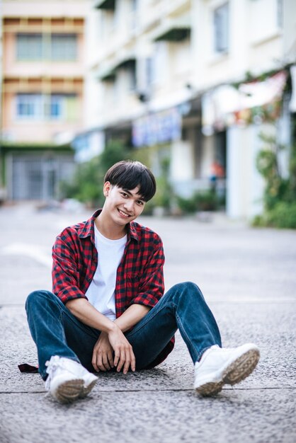 A young man in a striped shirt sitting on the street