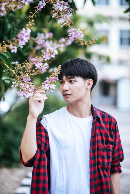 A young man in a striped shirt was standing on the roadside and holding the flower.