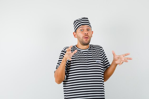 Young man in striped t-shirt hat keeping hands as holding or showing something and looking wondered  