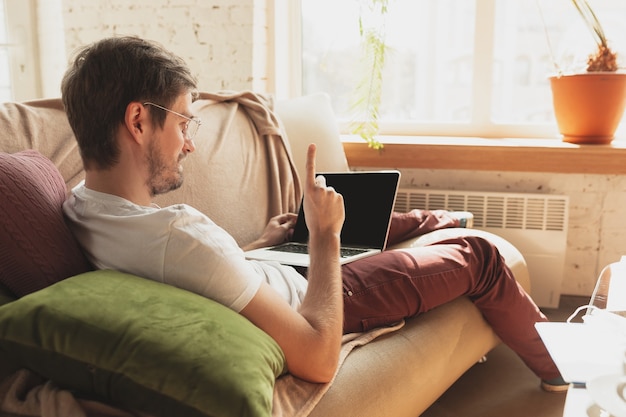 Free photo young man studying at home during online courses for journalist, critics, writers. getting profession while isolated, quarantine against coronavirus spreading. using laptop, smartphone, headphones.