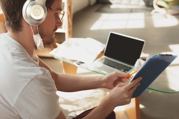 Free photo young man studying at home during online courses for laborer, journalist, developer. using laptop, smartphone, headphones.