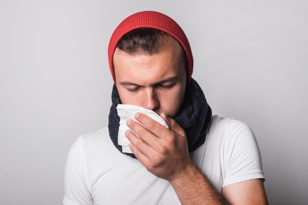 A young man suffering from cold and flu against gray background