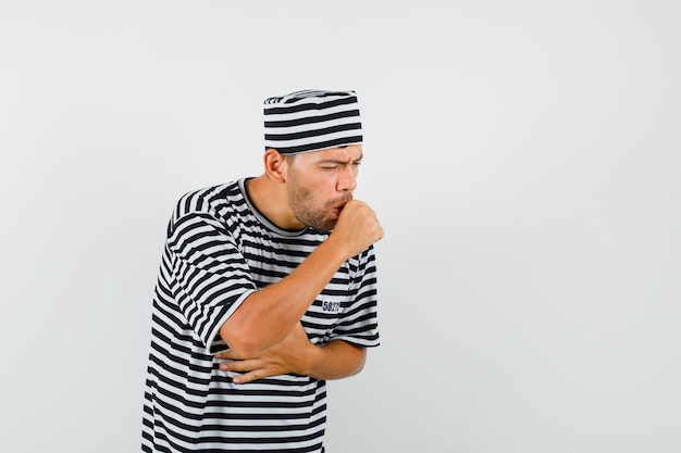 Free photo young man suffering from cough in striped t-shirt, hat and looking sick.