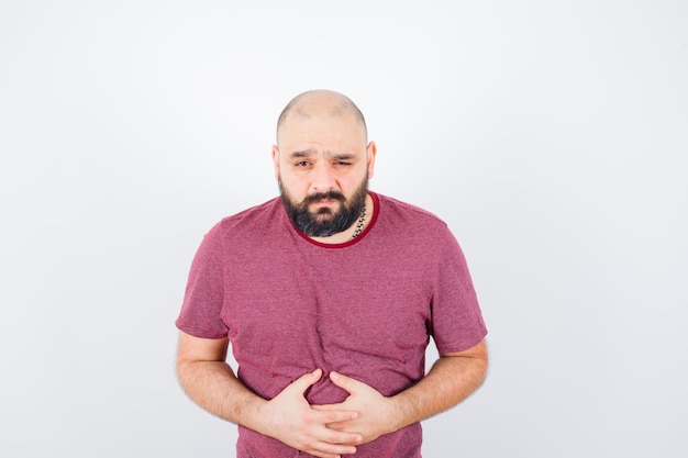 Young man suffering from stomach ache in pink t-shirt and looking painful. front view.