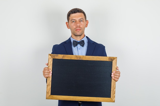 Free Photo young man in suit holding blackboard and looking serious 