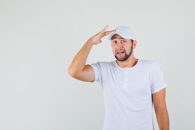 Young man in t-shirt,cap touching his cap and looking excited , front view.