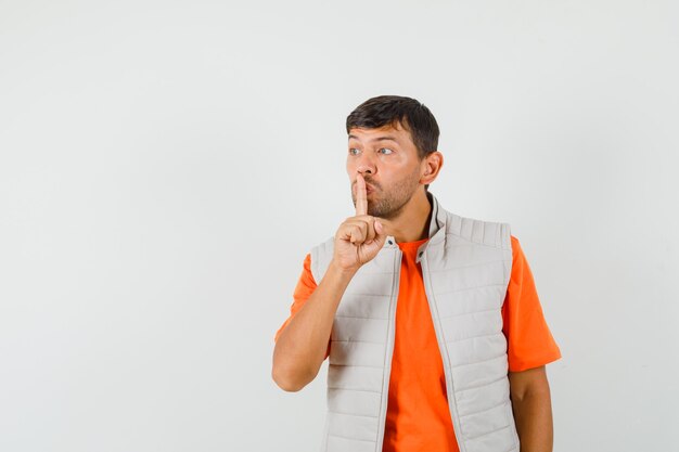 Young man in t-shirt, jacket showing silence gesture and looking careful , front view.