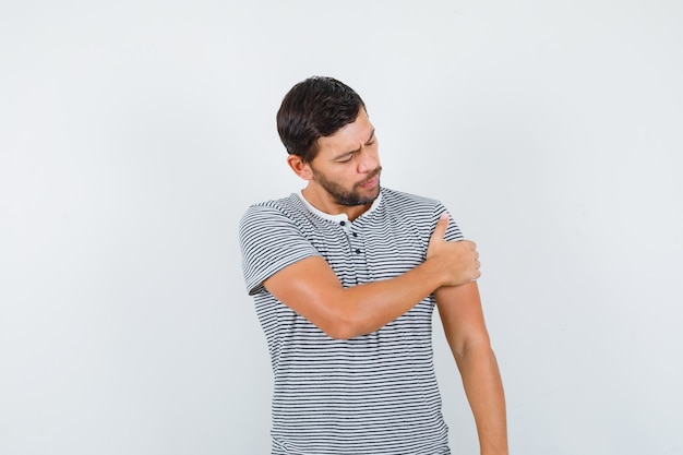 Young man in t-shirt keeping hand on arm and looking proud , front view.