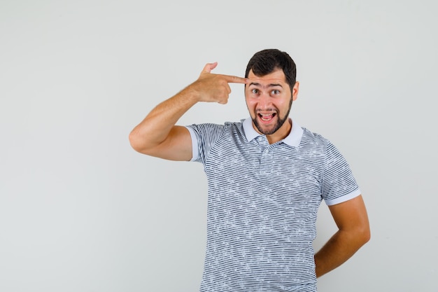 Young man in t-shirt making suicide gesture and looking amused , front view.