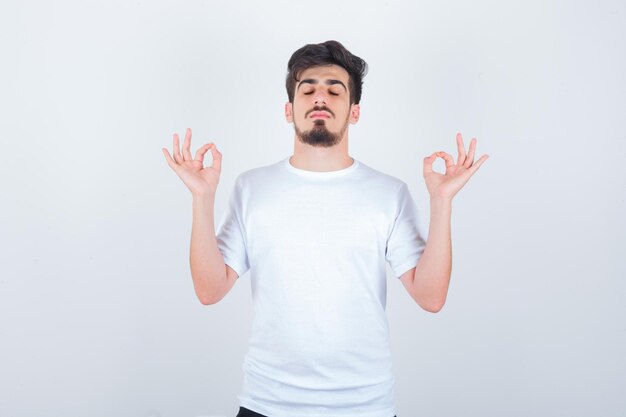 Young man in t-shirt showing meditation gesture and looking peaceful