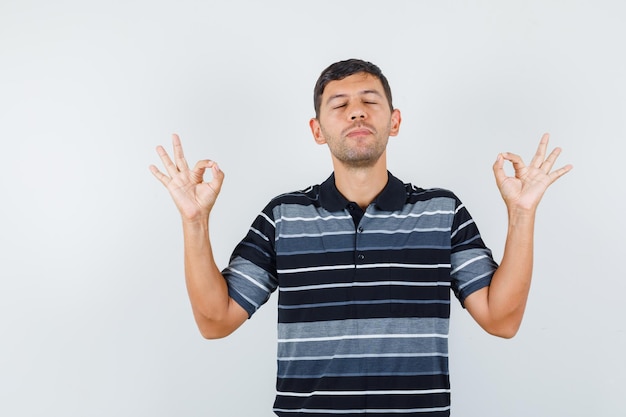 Young man in t-shirt showing ok gesture and looking peaceful , front view.