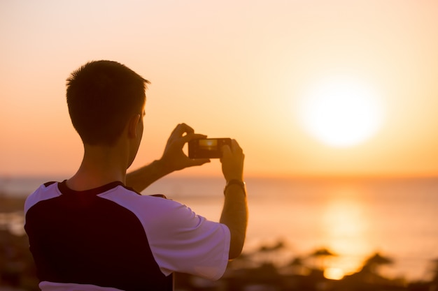 Free photo young man taking photo of sea sunset