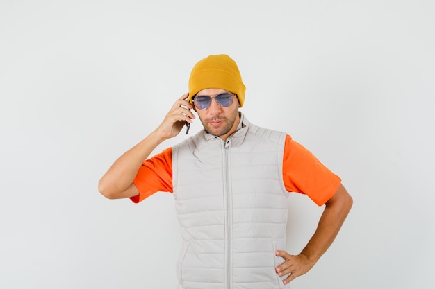 Free photo young man talking on mobile phone in t-shirt, jacket, hat and looking pensive.