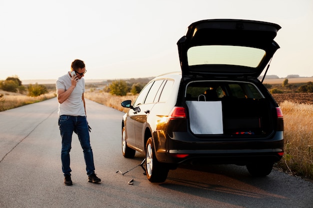 Young man talking on the phone  by a car