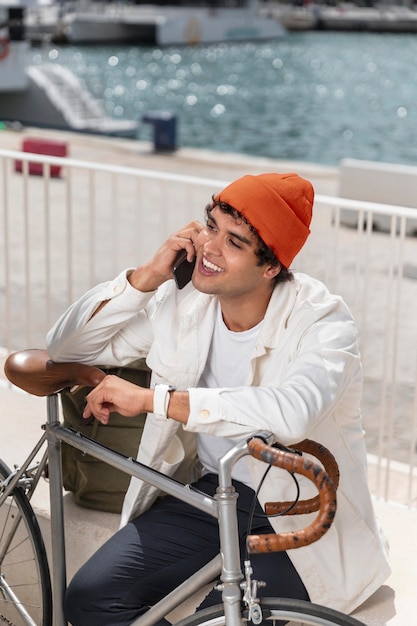 Free photo young man talking to the phone next to his bike