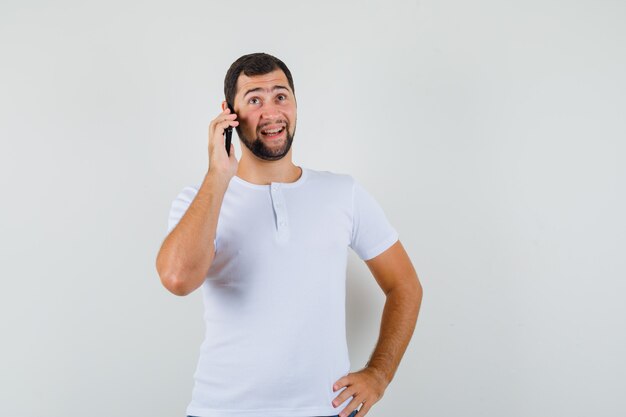 Young man talking on phone in white t-shirt and looking talkative , front view.