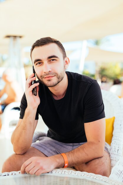 Young man talking a smartphone on the terrace by the sea. .