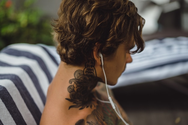 Free photo a young man in tattoos wearing headphones listens to music and draws in a notebook.