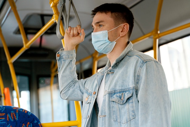 Young man travelling by city bus wearing surgical mask