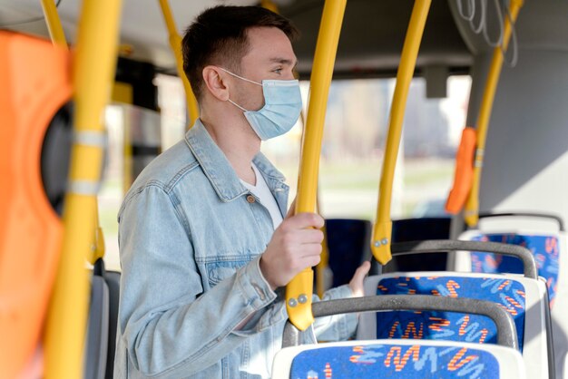 Young man travelling by city bus wearing surgical mask