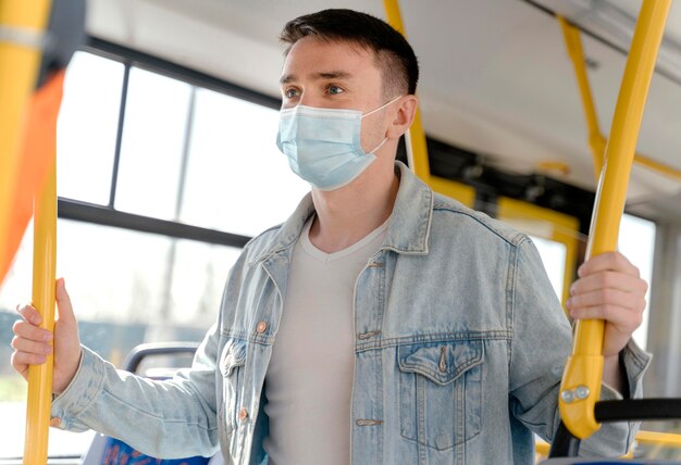 Young man travelling by city bus wearing surgical mask