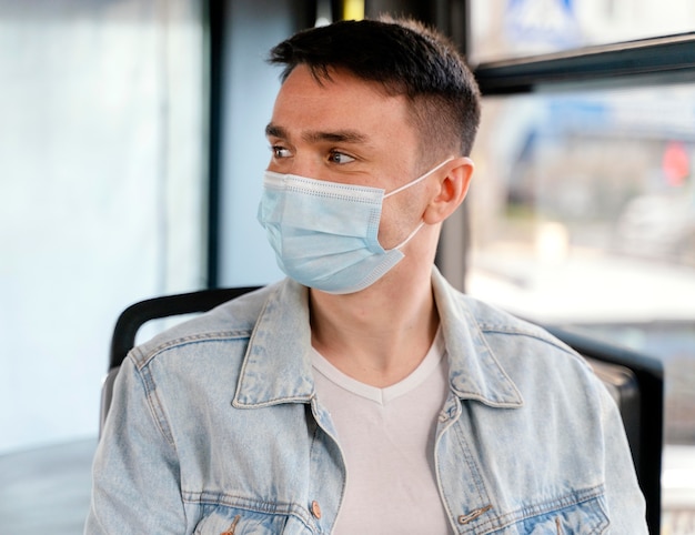 Young man travelling by city bus wearing surgical mask