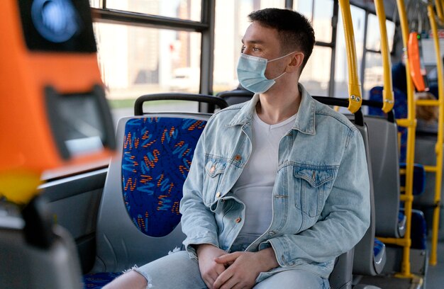 Young man travelling by city bus wearing surgical mask