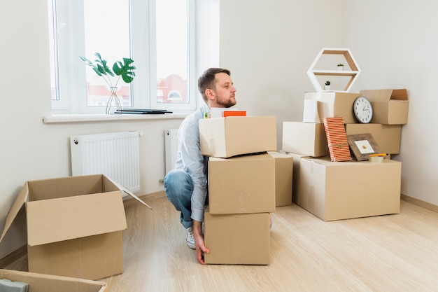 Young man trying to carry the stack of cardboard boxes at home