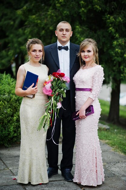 Young man in tuxedo posing with two girls in evening gowns on the graduation ceremony