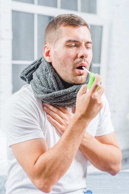 Young man using an analgesic spray to soften the throat