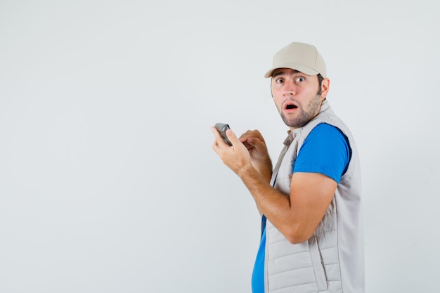 Young man using calculator in t-shirt, jacket and looking puzzled. .